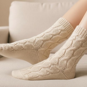 May include: Cream-coloured cable knit socks. The socks have a textured pattern and ribbed cuffs. They are made of a soft, warm material, ideal for colder weather. The socks are shown on a person's feet.