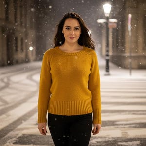 May include: A woman wearing a mustard yellow sweater and black pants stands on a snow-covered street at night. The sweater has a ribbed hem and cuffs. Snowflakes fall around her, and streetlights illuminate the scene.