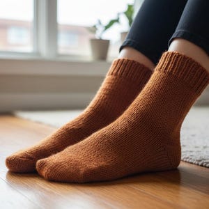 Op de afbeelding: Een paar gebreide sokken in een warme, aardse oranje tint. De sokken zijn dik en getextureerd, met geribbelde manchetten. Ze rusten op een houten vloer, wat duidt op comfort en warmte. De sokken zijn een gezellig accessoire.