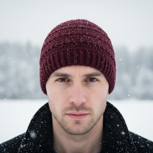 May include: A burgundy knit beanie is worn in a snowy outdoor setting. The hat is made of a textured material and is a deep red color. The person is wearing a black coat.
