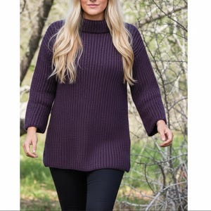 May include: A dark purple, ribbed knit jumper with a roll neck and long sleeves. The jumper is worn with black trousers. The model is walking outside with a blurred background of trees and foliage.