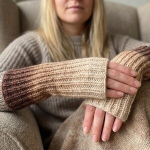 May include: Knitted fingerless gloves in a gradient of beige and brown tones. The gloves are made of a ribbed knit material and are designed to keep hands warm while leaving fingers free. The color transitions from light beige to a deep brown at the wrist.