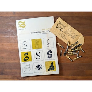 May include: A white Speedball Textbook 20th Edition for pen and brush lettering with a grid of letter S examples, accompanied by a tan paper envelope labeled Speedball Steel Brush and a collection of assorted metal calligraphy pen nibs.