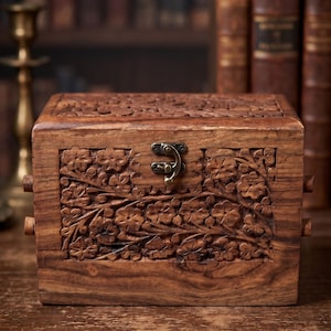 May include: A wooden box with intricate floral carvings. The box is rectangular with a hinged lid and a metal clasp. The wood has a warm, brown tone, and the carvings are detailed. The box is likely used for storing small items.