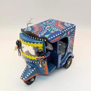 May include: A miniature, hand-painted blue auto rickshaw with intricate floral and geometric designs in red, white, and yellow. The decorative vehicle features small wheels and colorful tassels, showcasing a vibrant cultural aesthetic.
