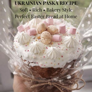 Puede incluir: Se muestra un pan Paska ucraniano tradicional para la Pascua. El pan horneado está cubierto con glaseado blanco, remolinos de merengue, malvaviscos de colores pastel y caramelos con forma de huevo moteado. El pan está envuelto en celofán transparente y atado con hilo.