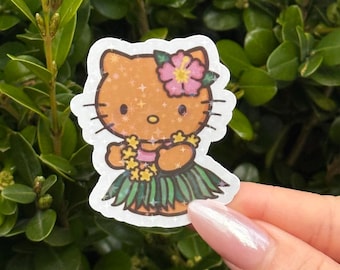 May include: A sticker featuring a cartoon cat in a hula skirt and flower lei. The cat is orange with black whiskers and a pink flower in its ear. The sticker is held against a background of green leaves.