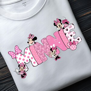 Puede incluir: Camiseta blanca con la palabra "MINNIE" en rosa, con personajes de Minnie Mouse. La "M" tiene lunares rosas grandes, y la "I" est&aacute; estampada con lazos. Un dise&ntilde;o juguet&oacute;n y colorido.