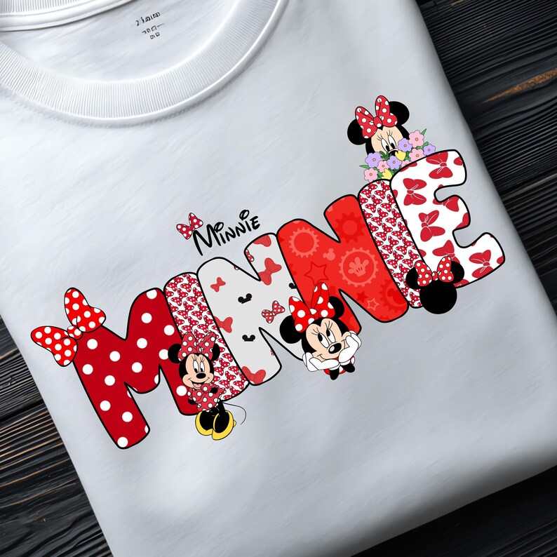 May include: A white t-shirt featuring the word MINNIE in large, stylized letters. The letters are filled with red and white polka dot patterns, floral motifs, and red geometric shapes. Minnie Mouse characters are integrated into the design.