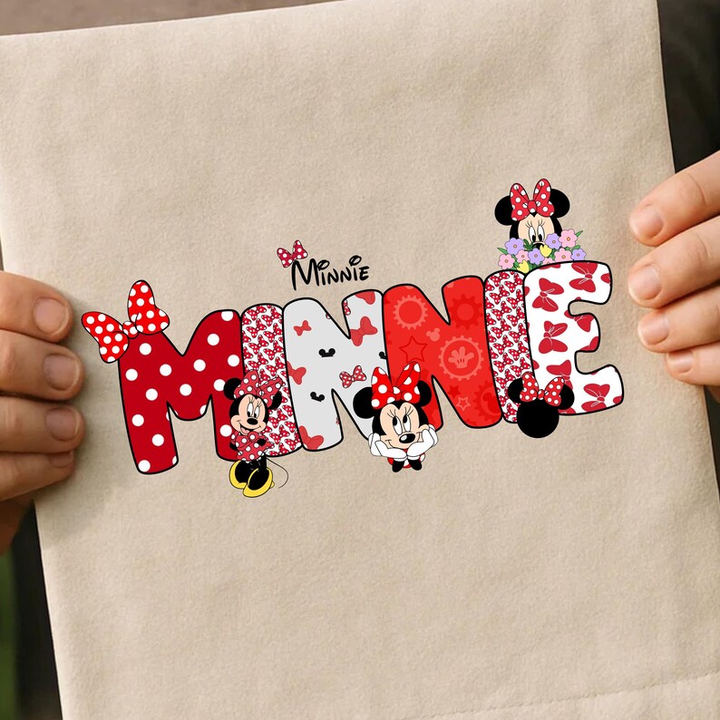 May include: A beige fabric surface featuring a graphic print of the word MINNIE in large, stylized letters. The letters are filled with red and white polka dot patterns, red floral motifs, and small bow designs. Minnie Mouse characters are integrated.