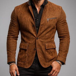 May include: A brown suede blazer with a black collar, a zippered chest pocket, and two front pockets. The blazer is buttoned and worn over a black shirt. The sleeves are long.