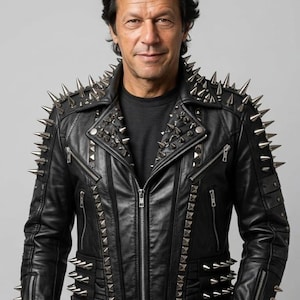 May include: A black leather jacket featuring silver-toned metal spikes on the shoulders, lapels, and sleeves. The jacket includes multiple zipped pockets, a central front zip closure, and additional rows of spikes along the lower sides.