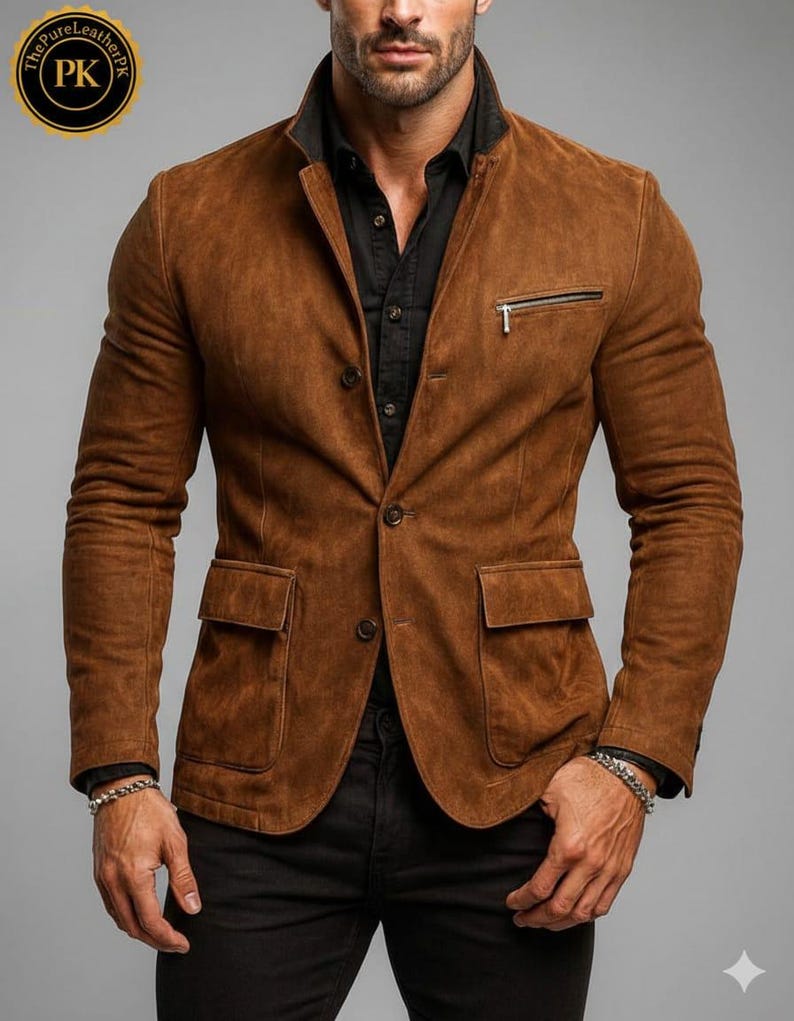 May include: A brown suede blazer with a black collar and a zippered chest pocket. The blazer has two front pockets and button closures. The sleeves are long and the fit is tailored. The blazer is worn over a black shirt.