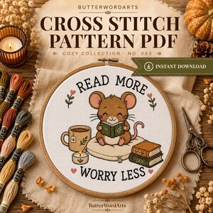 May include: A cross stitch pattern PDF titled READ MORE WORRY LESS featuring a brown mouse sitting on a cushion reading a book, with a mug, a candle, and a stack of books. The design is displayed in a wooden embroidery hoop on a fabric background.