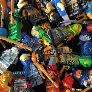 May include: A collection of colorful Lego Ninjago minifigures, featuring various characters in red, blue, green, and gold armor. The figures are equipped with weapons like swords and staffs, creating a dynamic and action-packed scene.