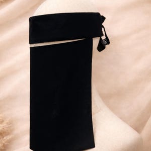 May include: Black niqab veil, featuring a wide headband and a long, rectangular face covering. The veil is displayed on a mannequin head against a soft, neutral background. The fabric appears to be opaque.