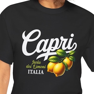 May include: Black t-shirt featuring the word "Capri" in white script above a branch of lemons. Below the lemons are the words "Isola dei Limoni" and "ITALIA" in white text. The lemons are yellow with green leaves.