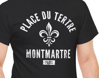 May include: A black short-sleeved t-shirt featuring a white distressed graphic print. The design includes a fleur-de-lis symbol centered between the text PLACE DU TERTRE above and MONTMARTRE PARIS below, with PARIS enclosed in a rectangular box.