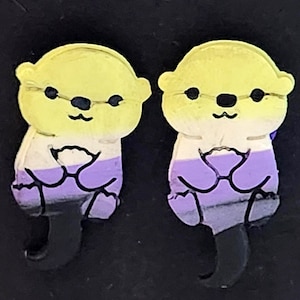 May include: A pair of stud earrings shaped like otters. Each otter features a horizontal color gradient pattern consisting of yellow at the top, white in the middle, purple below, and black at the bottom, with black outlines defining the features.