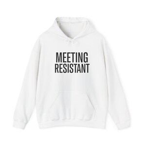 Puede incluir: Sudadera con capucha blanca con bolsillo delantero y cordón. El texto "MEETING RESISTANT" está impreso en letras negras en el pecho. Una prenda casual y cómoda.