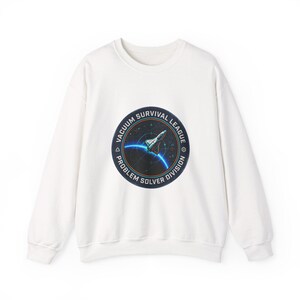 May include: A white crewneck sweatshirt featuring a circular graphic with the text "VACUUM SURVIVAL LEAGUE PROBLEM SOLVER DIVISION." The graphic depicts a spaceship and a blue planet. The sweatshirt is a casual garment.