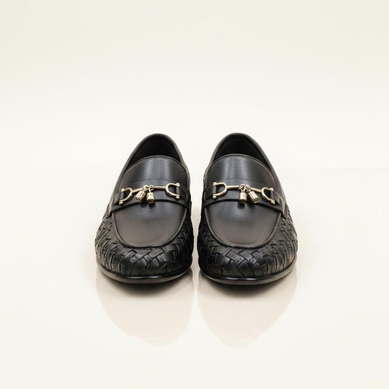 May include: A pair of black leather loafers with gold-colored hardware. The front of the shoe features a woven design, while the top has a smooth finish with a decorative metal buckle.