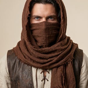 May include: A dark brown textured fabric hood and face covering scarf with frayed edges. The scarf is draped over the head and wrapped around the lower face, featuring a lightweight, crinkled material that provides full coverage.