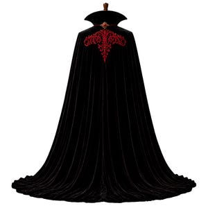 May include: A floor-length black velvet cape featuring a high standing collar and a red embroidered floral pattern across the upper back. The garment includes a decorative red jewel clasp at the neckline, creating a structured and flowing silhouette.