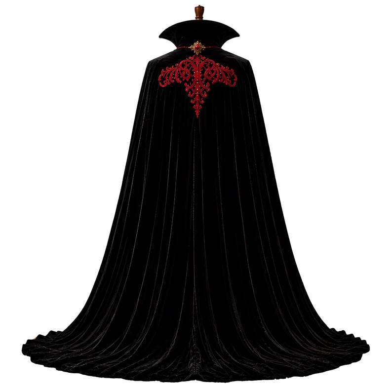 May include: A floor-length black velvet cape featuring a high standing collar and a red embroidered floral pattern across the upper back. The garment includes a decorative red jewel clasp at the neckline, creating a structured and flowing silhouette.