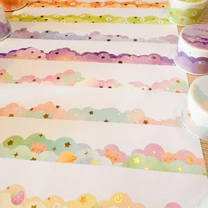 May include: Decorative washi tape rolls with colorful cloud and star designs. The tape features various pastel colors, including pink, purple, green, and orange. Some rolls have cute illustrations of bears, bunnies, and strawberries. Perfect for scrapbooking and crafts.