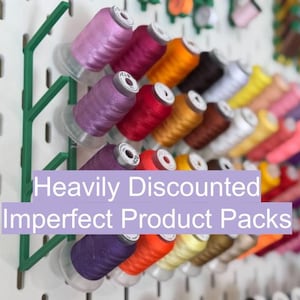May include: A white pegboard wall organizer featuring green plastic racks holding numerous spools of multi-colored embroidery thread. The text "Heavily Discounted Imperfect Product Packs" is overlaid in white on a light purple rectangular background.