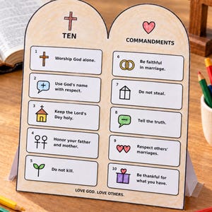 May include: A tabletop sign shaped like stone tablets featuring the Ten Commandments with colorful icons and text. The sign lists ten numbered rules, includes a cross and heart symbol at the top, and displays the text LOVE GOD. LOVE OTHERS. at the bottom.
