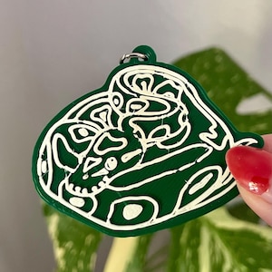 May include: A dark green keychain featuring a white line art design of a coiled snake. The snake is depicted in a continuous, abstract style with visible texture from the 3D printing process. A small metal ring is attached to the top loop.