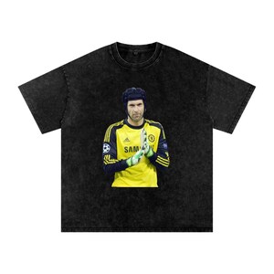 Peut inclure: T-shirt noir avec un graphisme d'un gardien de but en maillot jaune et détails bleus. Le gardien porte un casque et des gants. Le maillot porte le mot "SAM".