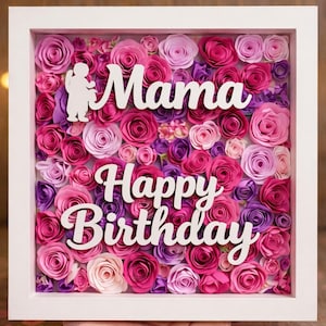 May include: A framed floral art piece with a white border. The artwork features a dense arrangement of paper roses in shades of pink, purple, and magenta. White text spells out "Mama Happy Birthday", with a silhouette of a child.