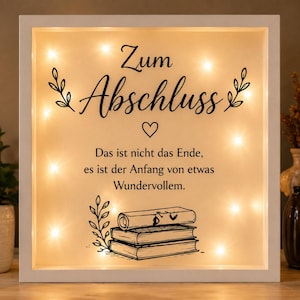 Könnte beinhalten: Ein weiß gerahmtes, beleuchtetes Schild mit den Worten "Zum Abschluss" und einem Herzsymbol. Darunter steht der Text: "Das ist nicht das Ende, es ist der Anfang von etwas Wundervollem." Das Schild hat Lichterketten und eine Zeichnung von Büchern.