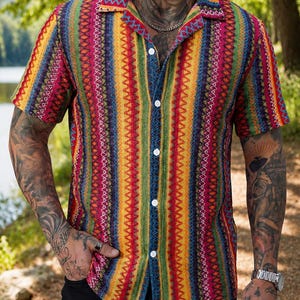 May include: A short-sleeve button-down shirt featuring a vibrant, multi-colored vertical striped pattern. The design incorporates repeating geometric zig-zag lines in shades of red, yellow, green, and blue, finished with a classic collar.