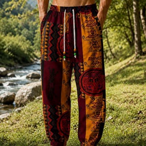 May include: Loose-fitting trousers featuring a vibrant patchwork pattern in shades of deep red, mustard yellow, and black. The fabric displays intricate tribal-inspired motifs and circular designs, finished with an elastic waistband and white drawstring.