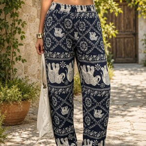 May include: High-waisted navy blue trousers featuring a repeating white elephant and floral geometric pattern. The trousers have an elasticated waistband and elasticated cuffs at the ankles, paired with a plain white crop top and a white tote bag.