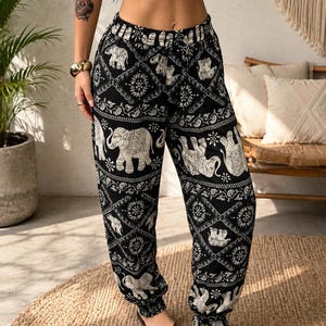 May include: Black and white joggers featuring a repeating pattern of elephants and intricate geometric diamond shapes. The trousers have an elasticated waistband with a drawstring tie and elasticated cuffs at the ankles, providing a relaxed fit.