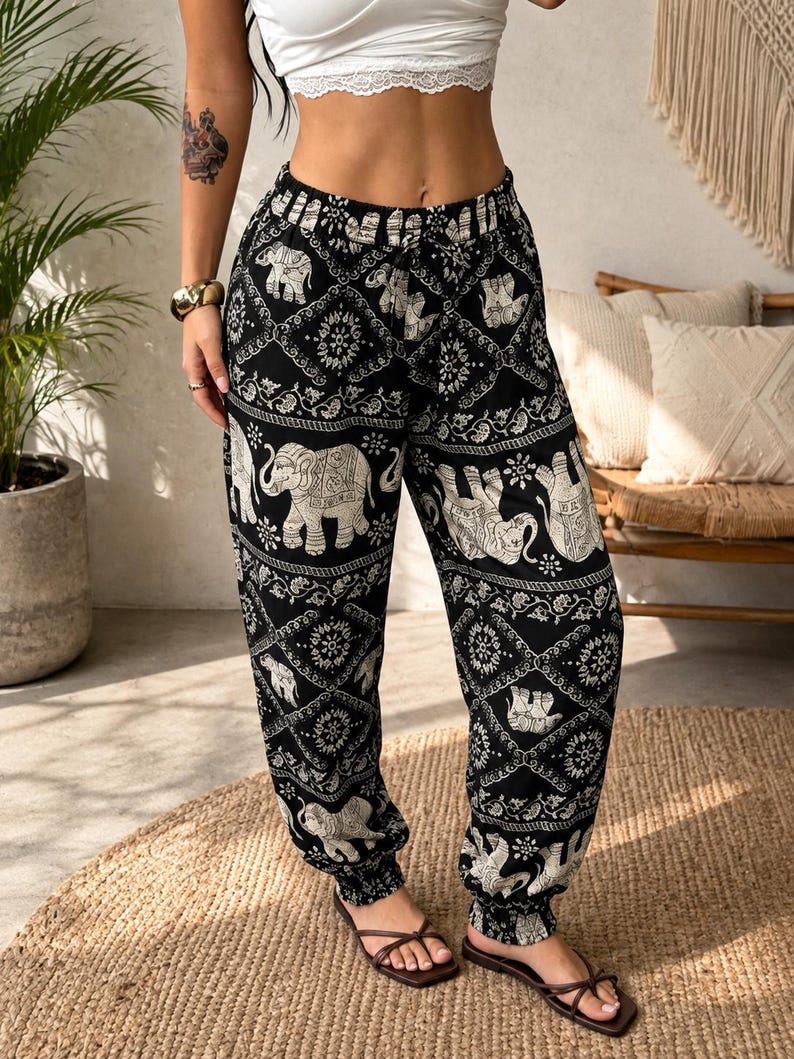 May include: Black and white joggers featuring a repeating pattern of elephants and intricate geometric diamond shapes. The trousers have an elasticated waistband with a drawstring tie and elasticated cuffs at the ankles, providing a relaxed fit.
