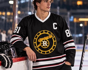 May include: A black hockey jersey with white V-neck collar, featuring the number 81 on the sleeves and a large circular logo on the chest depicting a yellow cannon and the letter R. A white letter C is on the upper left chest, with white and red stripes.