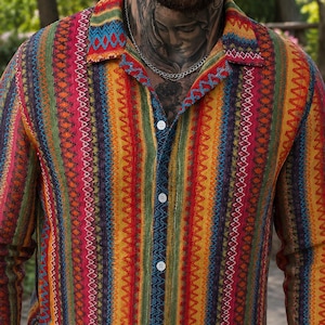 May include: A long-sleeved button-down shirt featuring a vibrant, multi-colored vertical striped pattern. The design incorporates repeating geometric motifs in shades of red, yellow, green, orange, and blue, finished with a classic collar.