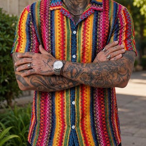 May include: A short-sleeved button-down shirt featuring a vibrant, vertical striped pattern in shades of red, yellow, green, and blue. The shirt has a classic collar and white buttons running down the center front, with a textured, woven appearance.