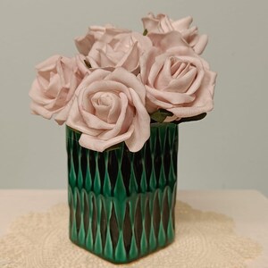 May include: A bouquet of pale pink roses arranged in a cylindrical green vase with a vertical, textured, diamond-shaped pattern. The vase features a glossy finish with dark green accents in the recessed areas and lighter green on the raised ridges.