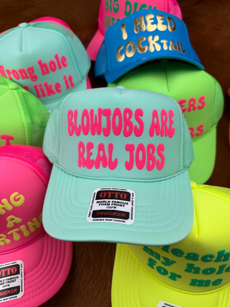 May include: A collection of trucker hats in various colors, including teal, pink, blue, and green. Each hat features bold, eye-catching text in contrasting colors. The hats have a mesh back and a foam front, with a snap closure.
