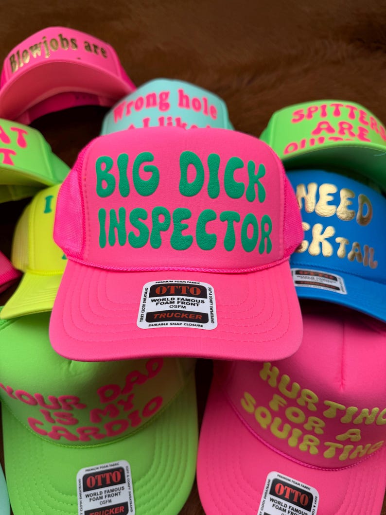 May include: A collection of trucker hats in various neon colors, including pink, green, and blue. Each hat features bold, humorous text in contrasting colors. The hats have a mesh back and a foam front, with a snap closure.