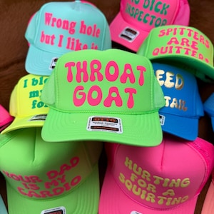 May include: A collection of trucker hats in various bright colors, including green, pink, blue, and yellow. Each hat features bold text in contrasting colors. The phrases include "Throat Goat," "Big Dick Inspector," and "Hurting for a Squirtin."