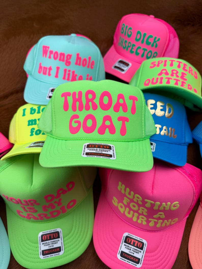 May include: A collection of trucker hats in various bright colors, including green, pink, blue, and yellow. Each hat features bold text in contrasting colors. The phrases include "Throat Goat," "Big Dick Inspector," and "Hurting for a Squirtin."