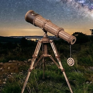 May include: A wooden telescope with a brown leather eyepiece sits on a tripod, with a decorative circular pendant hanging from it. The telescope is set against a backdrop of a starry night sky and a landscape of hills and trees.